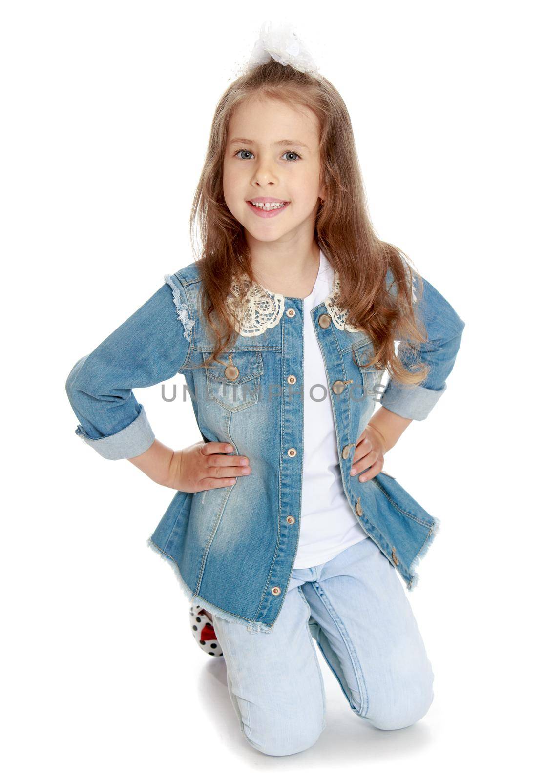 Nice little girl in denim suit. The girl kneeling on the floor. She smiles sweetly at the camera - Isolated on white background