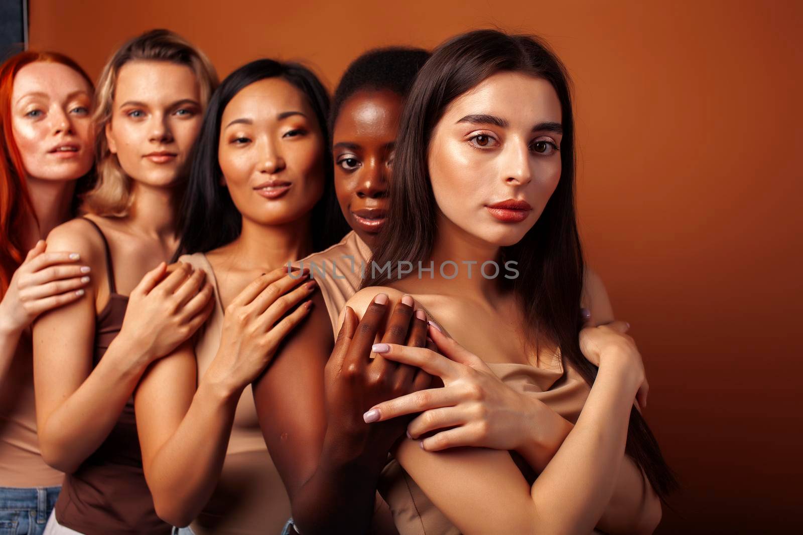 young pretty caucasian, afro, scandinavian woman posing cheerful together on brown background, lifestyle diverse nationality people concept close up