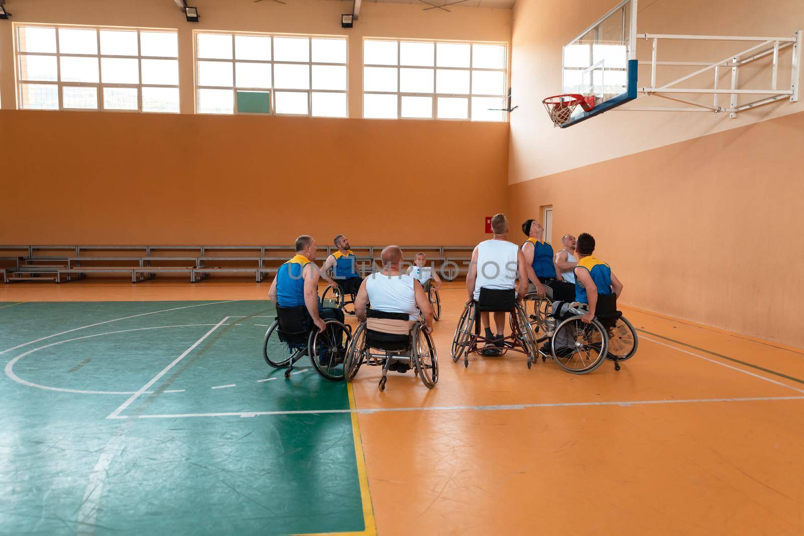 Disabled War veterans mixed race and age basketball teams in wheelchairs playing a training match in a sports gym hall. Handicapped people rehabilitation and inclusion concept by dotshock