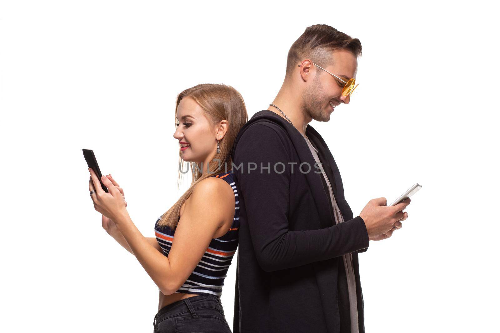 Man and woman stand with their backs to each other with telephones in their hands on white background. Studio shot