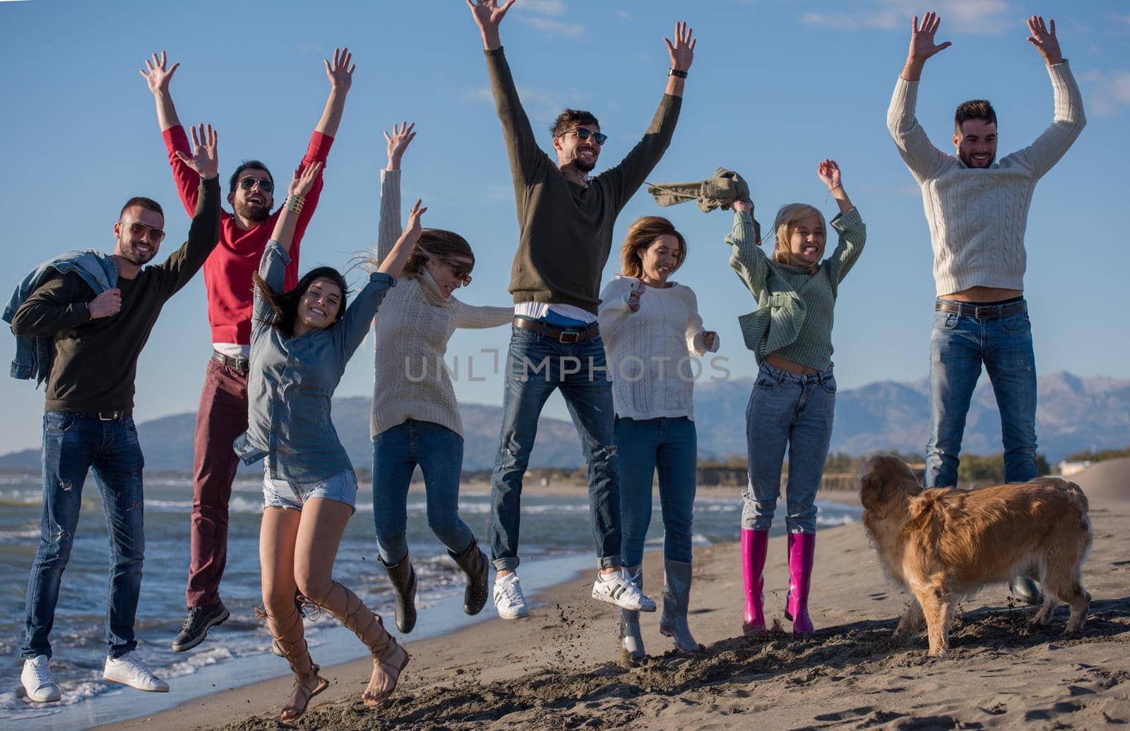 Group of excited young friends jumping together at sunny autumn beach