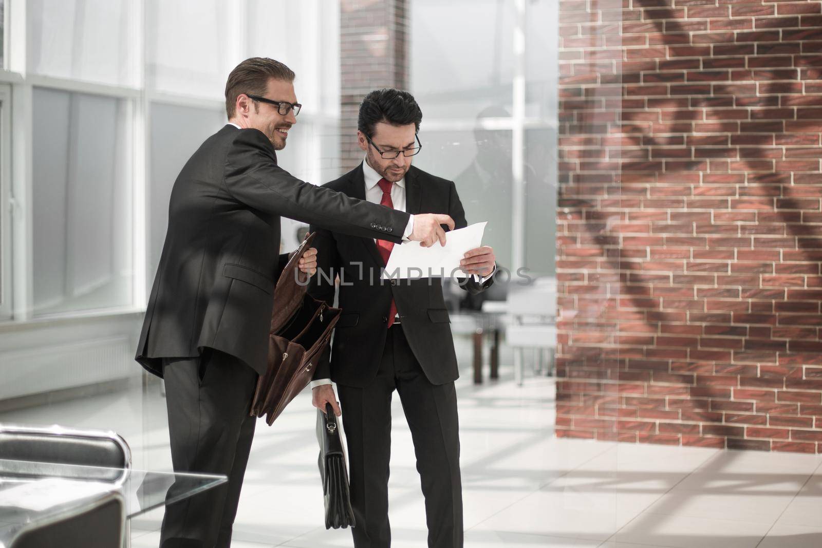 two businessmen discuss the document standing in the office lobby. by asdf