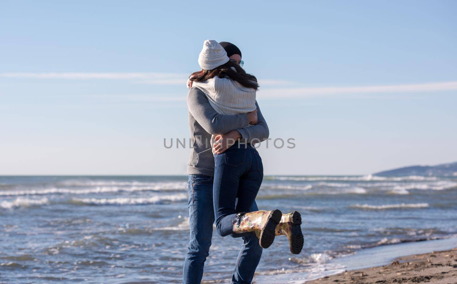 Young couple having fun walking and hugging on beach during autumn sunny day