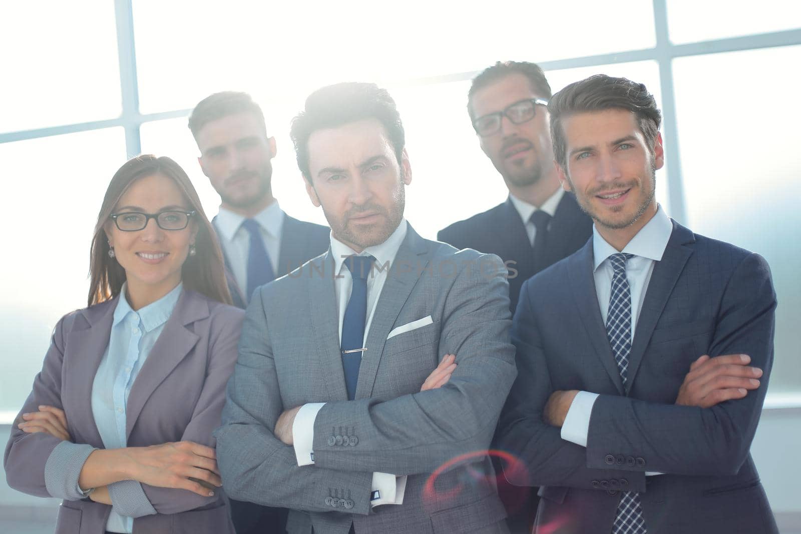 Team of successful happy businesspeople standing in office, businesswoman in front smiling.