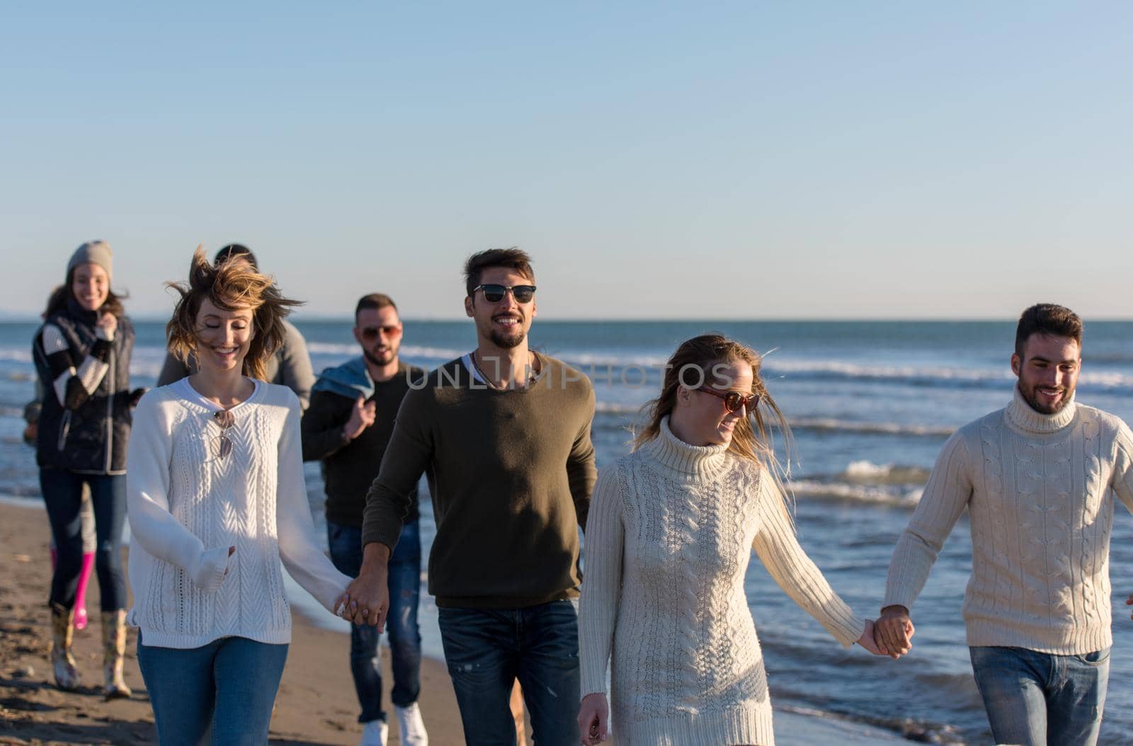 group of young friends spending day together running on the beach during autumn day