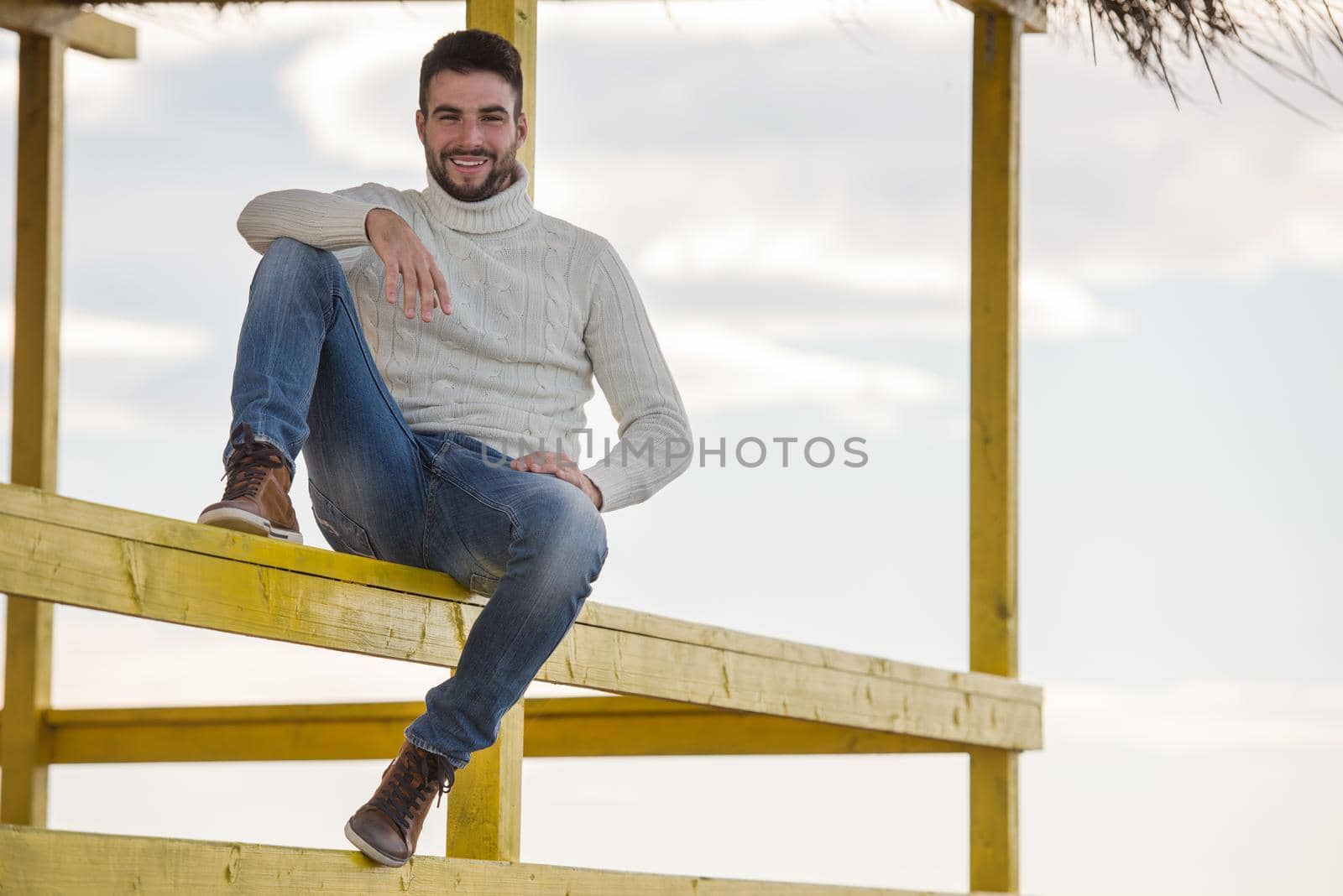 Young man on the beach. The guy enjoying the warm autumn day. Portrait of man near the water