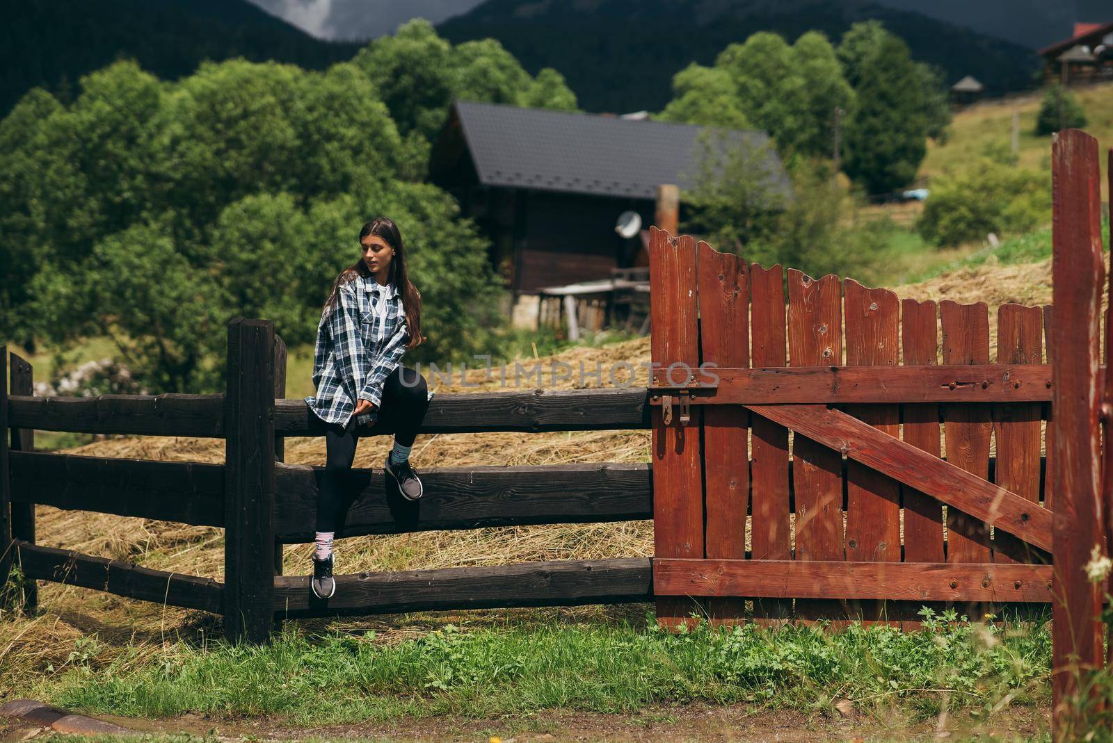 A young attractive Caucasian female sitting on a fence and posing at camera