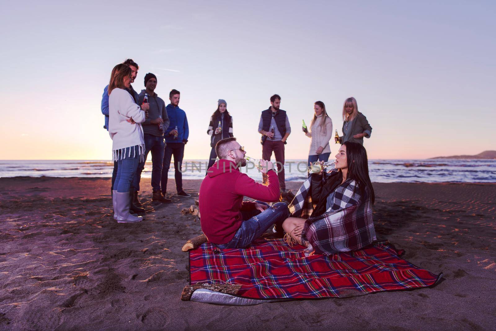 Young Couple enjoying with friends Around Campfire on The Beach At sunset drinking beer