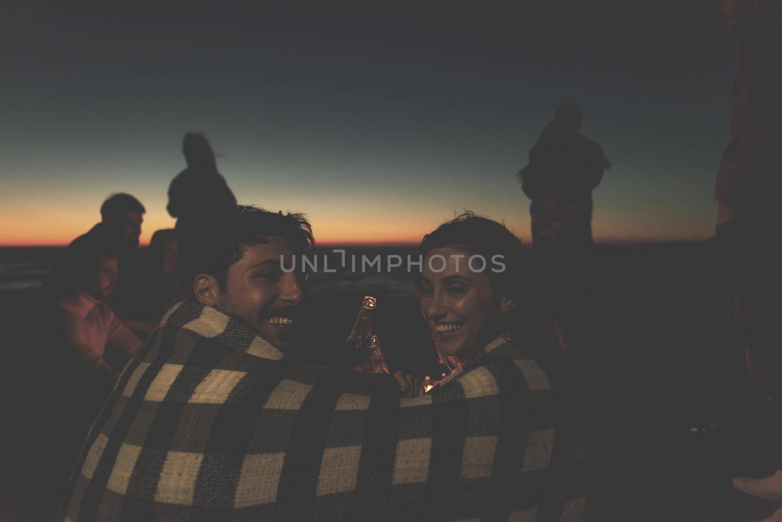Young Couple enjoying with friends Around Campfire on The Beach At sunset drinking beer