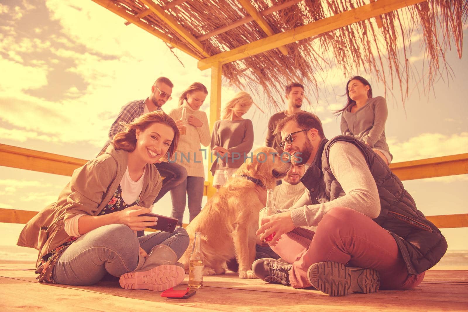 Happy Group Of Friends Hanging Out At Beach House having fun and drinking beer on autumn day