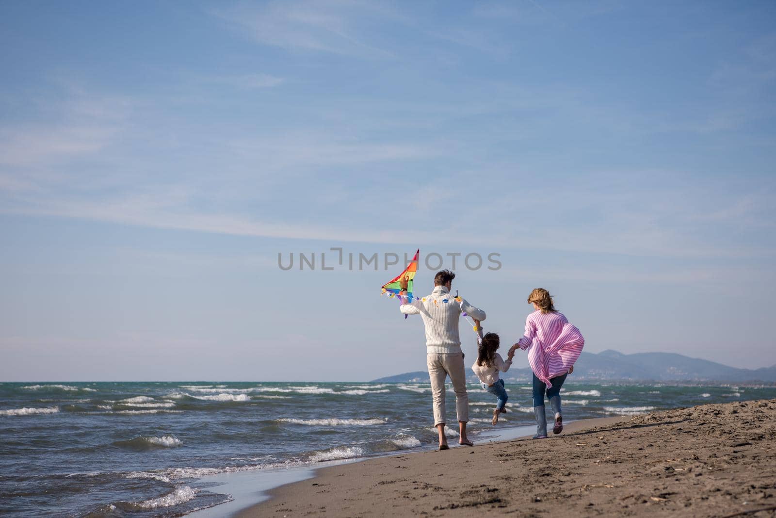 young family with kids resting and having fun with a kite at beach during autumn day