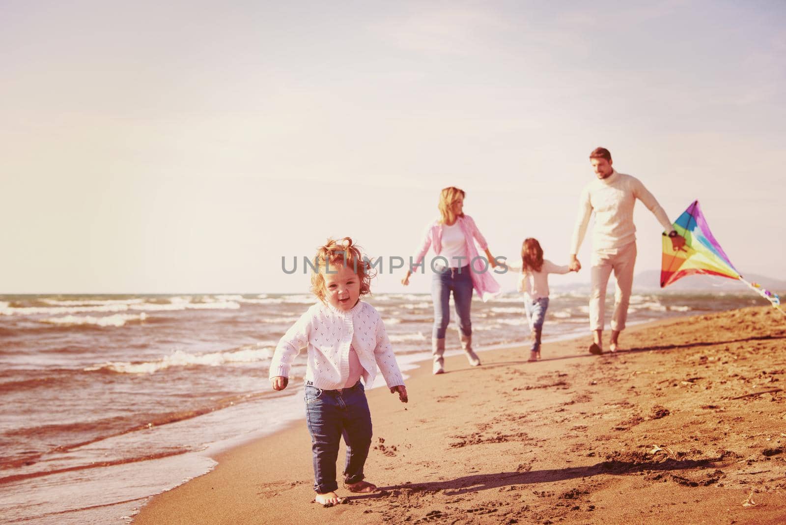 young family with kids resting and having fun with a kite at beach during autumn day filter