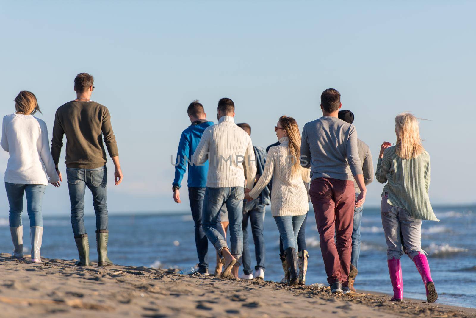 Group of friends running on beach during autumn day by dotshock