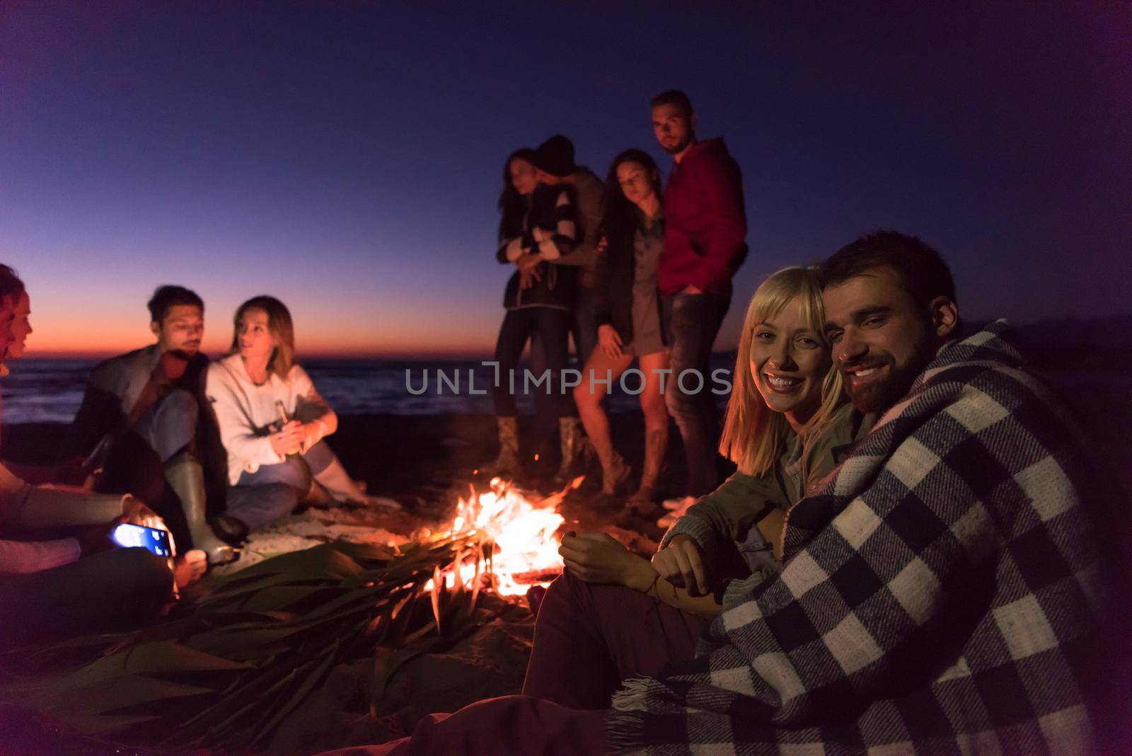 Young Couple enjoying with friends Around Campfire on The Beach At sunset drinking beer