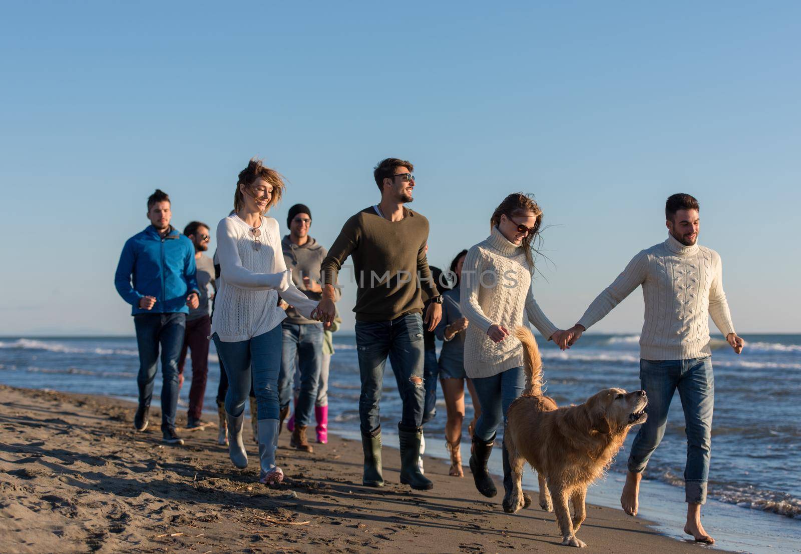 group of young friends spending day together running on the beach during autumn day