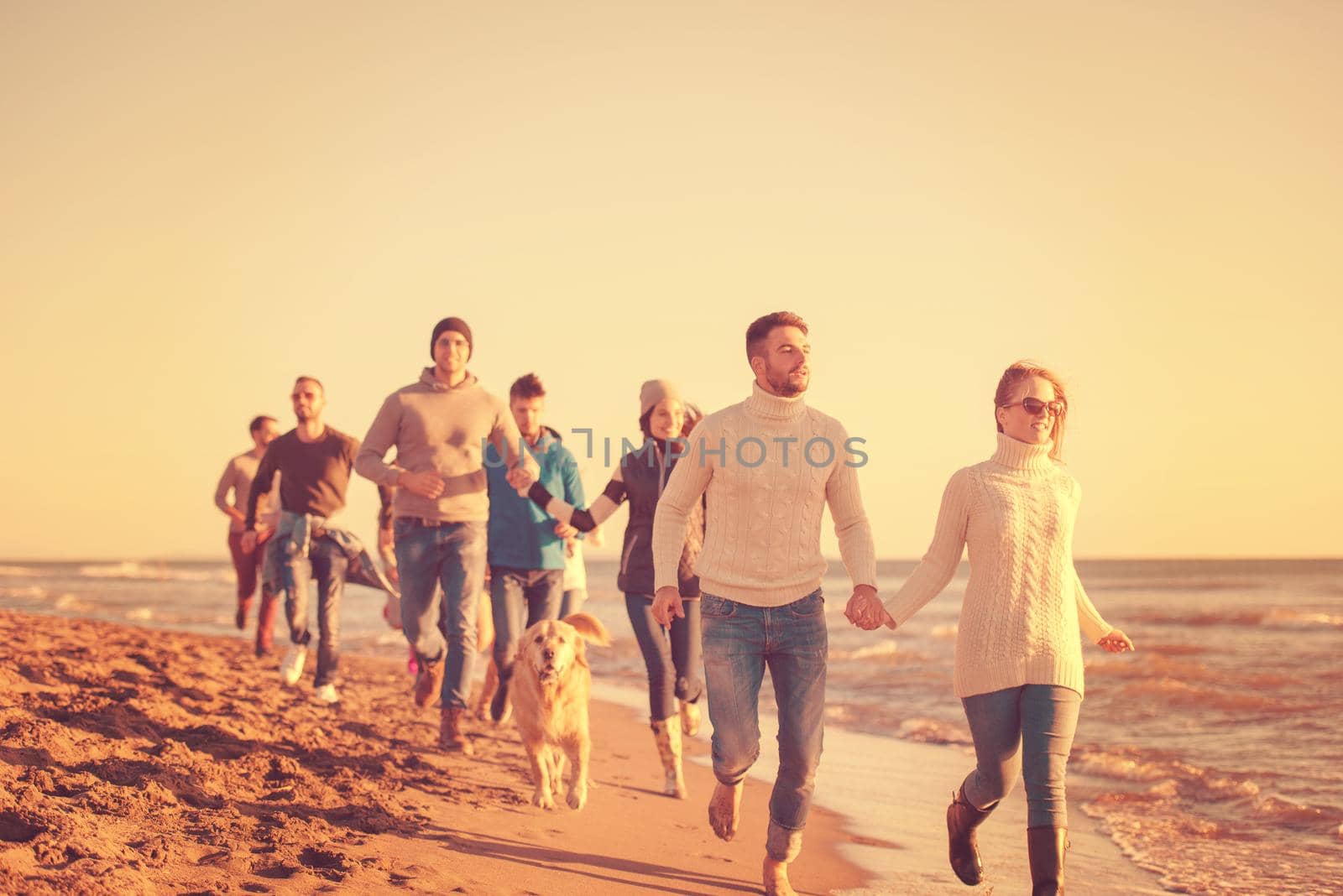 group of young friends spending day together running on the beach during autumn day