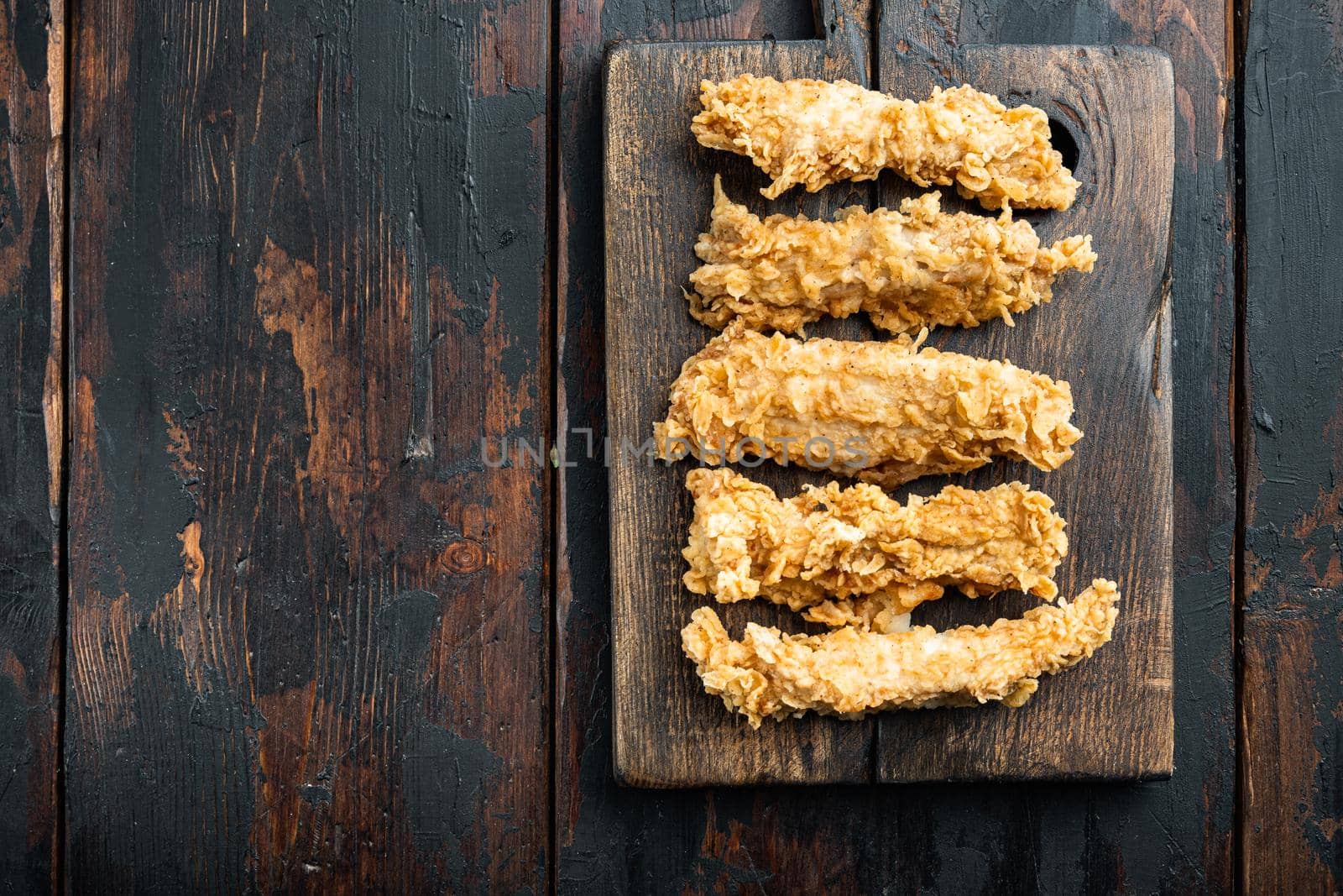 Fried crispy chicken stripes parts on old dark wooden table, top view, with copy space.