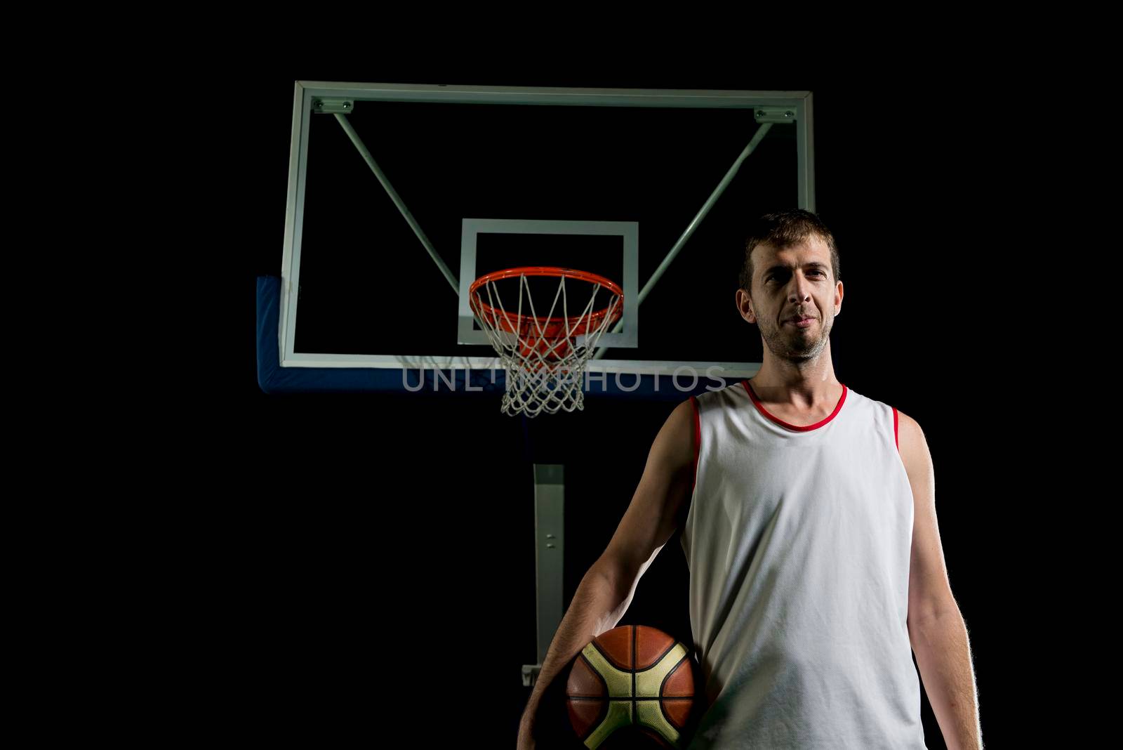 Basketball player portrait  on basketball court holding ball with black isolated background