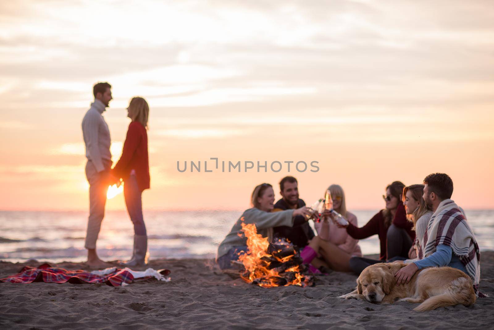 Young Couple enjoying with friends Around Campfire on The Beach At sunset drinking beer