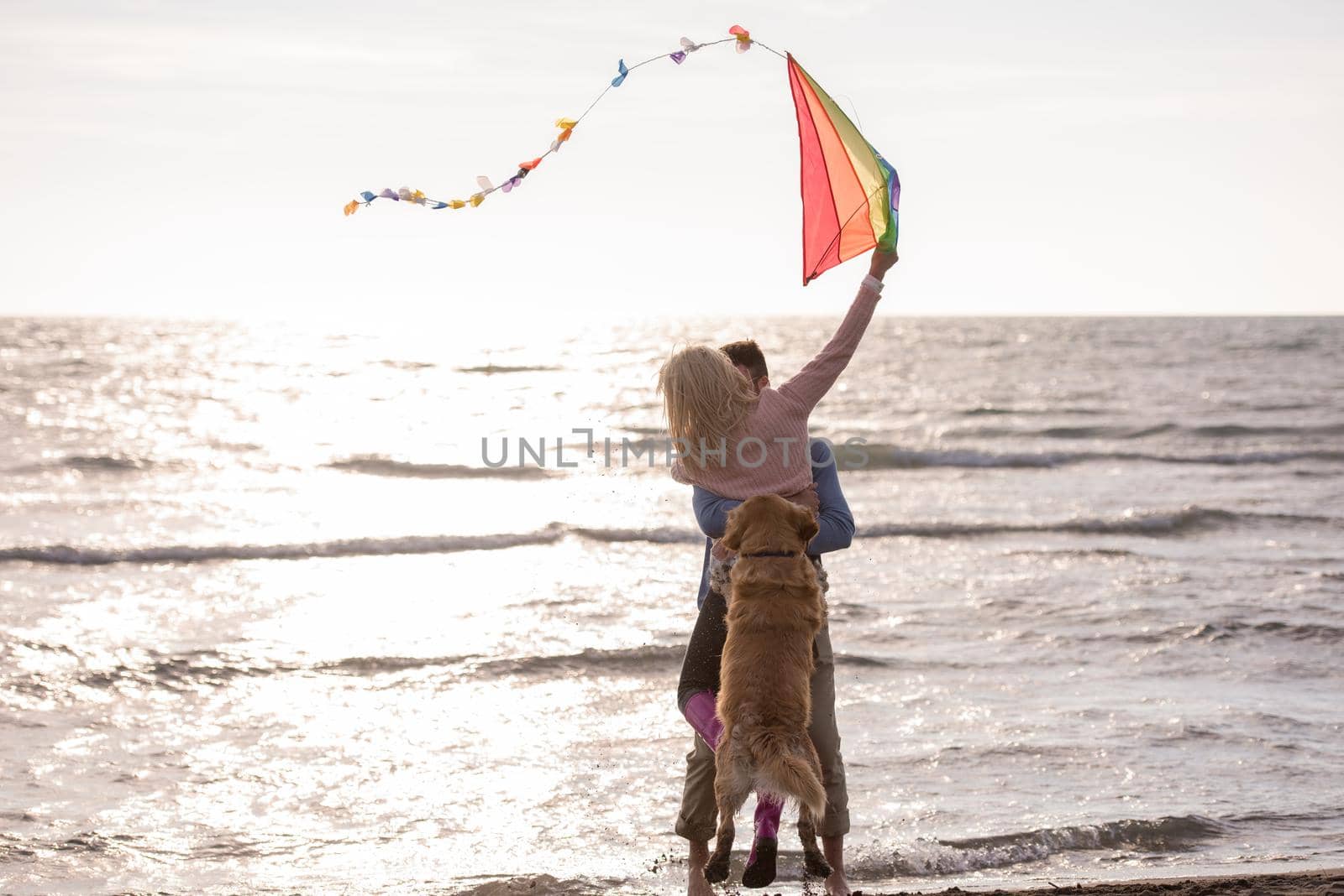 Young Couple having fun playing with a dog and Kite on the beach at autumn day