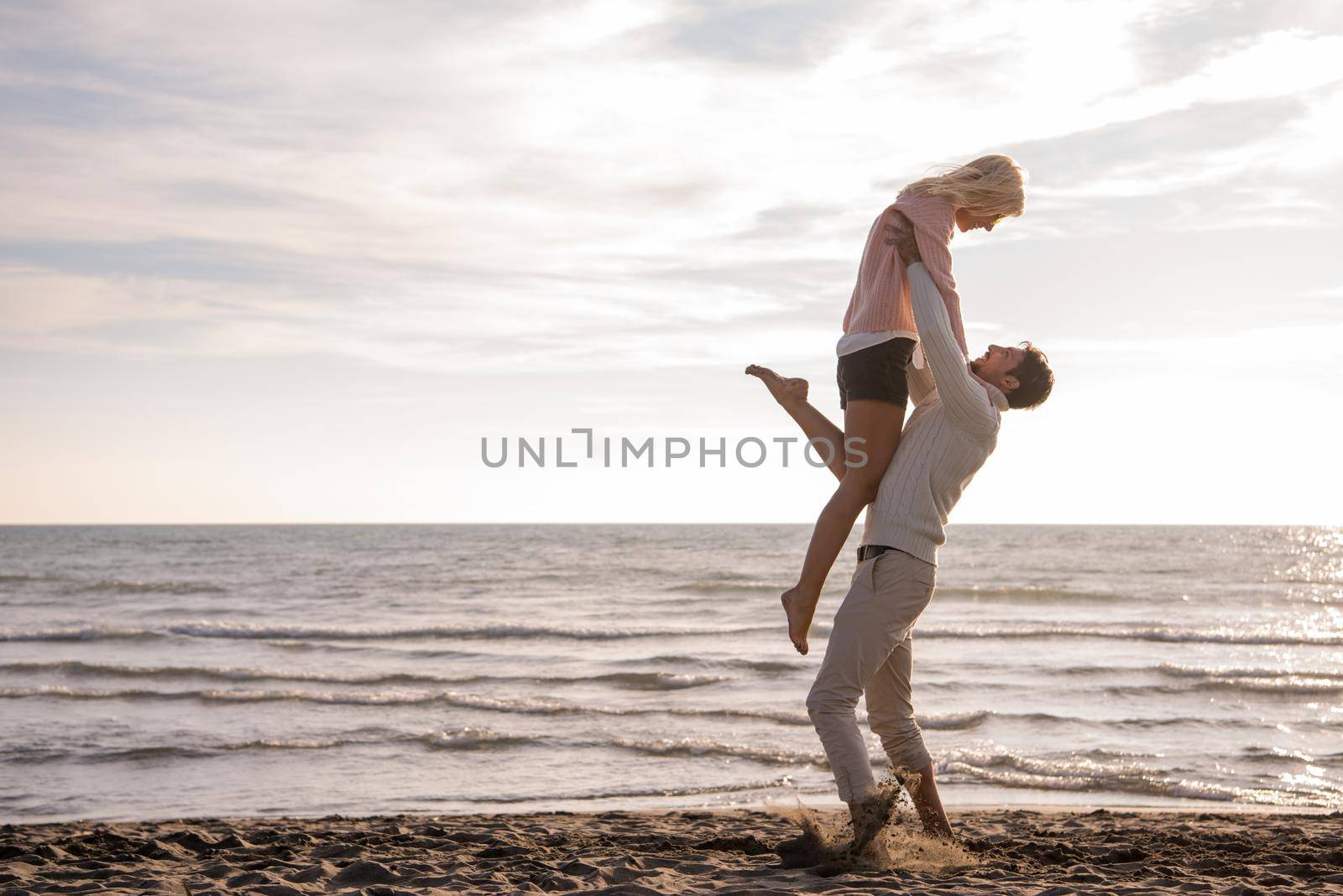 Young couple having fun walking and hugging on beach during autumn sunny day