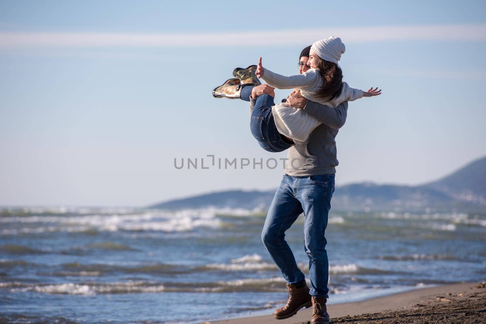 Young couple having fun walking and hugging on beach during autumn sunny day