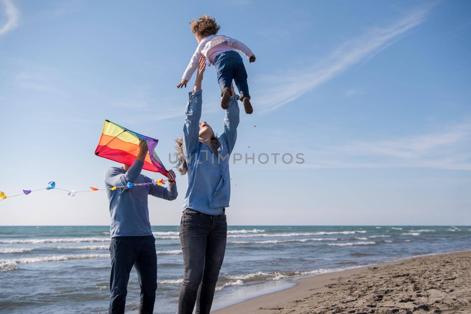 young family with kids resting and having fun with a kite at beach during autumn day