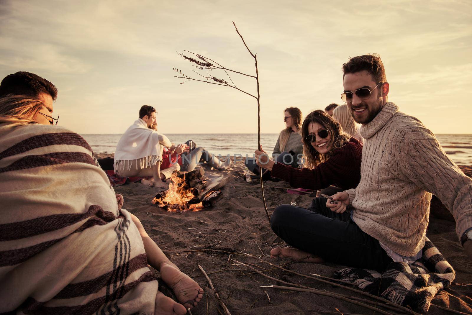 Young Couple enjoying with friends Around Campfire on The Beach At sunset drinking beer filter