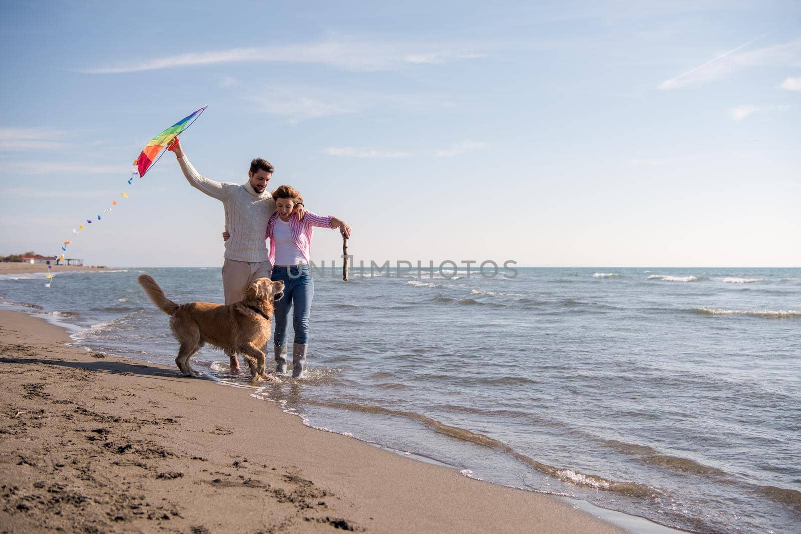 Young Couple having fun playing with a dog and Kite on the beach at autumn day