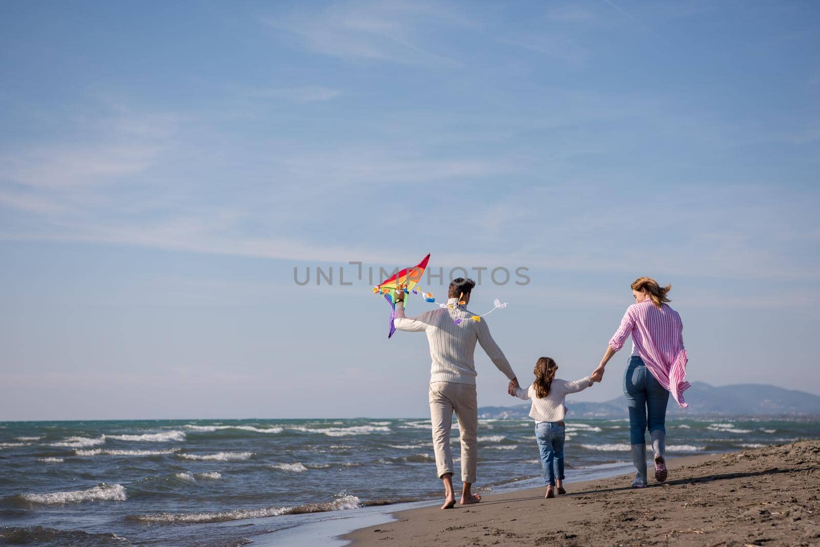 young family with kids resting and having fun with a kite at beach during autumn day