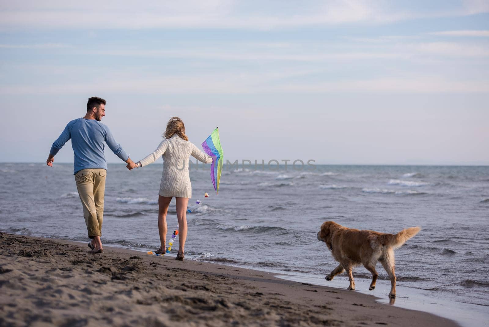 Young Couple having fun playing with a dog and Kite on the beach at autumn day