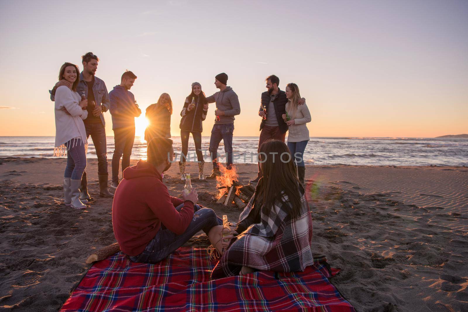 Young Couple enjoying with friends Around Campfire on The Beach At sunset drinking beer