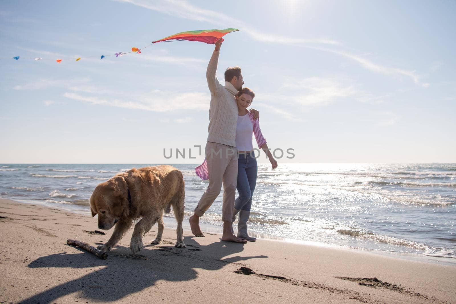 Young Couple having fun playing with a dog and Kite on the beach at autumn day