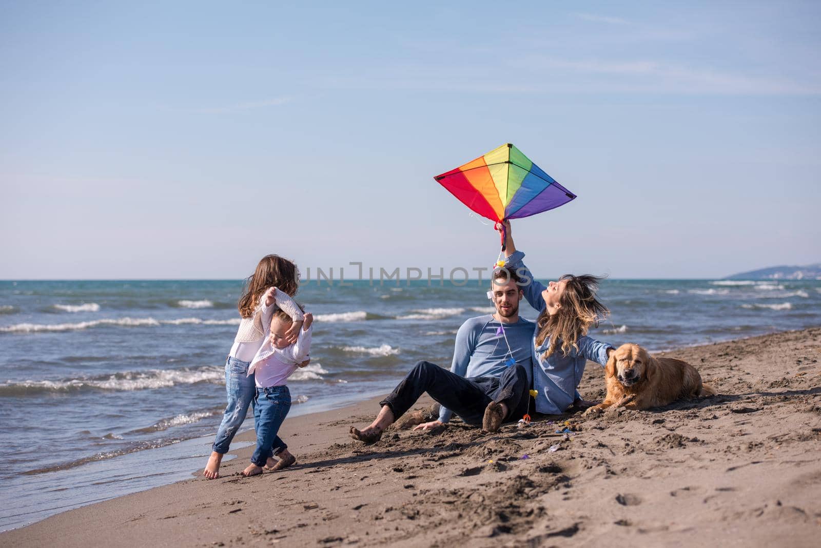 happy young family with kids having fun with a dog and  kite at beach during autumn day