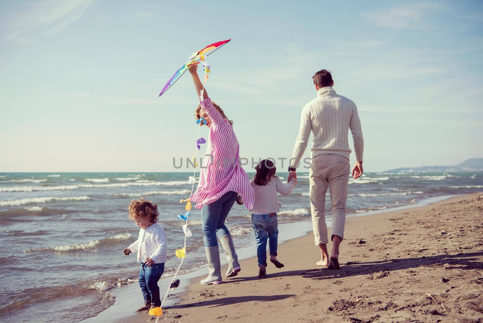 young family with kids resting and having fun with a kite at beach during autumn day filter