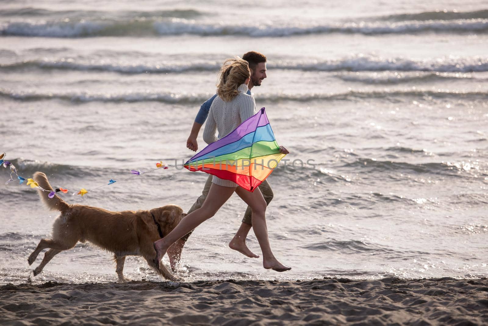 Young Couple having fun playing with a dog and Kite on the beach at autumn day