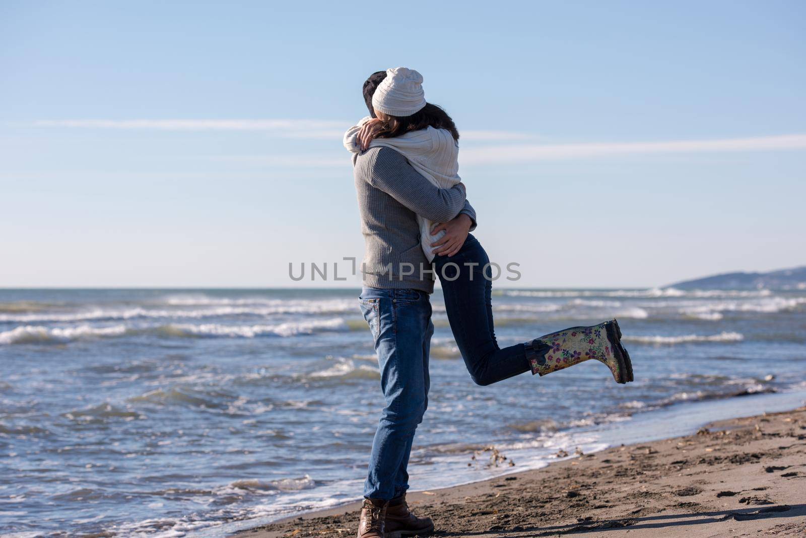 Young couple having fun walking and hugging on beach during autumn sunny day