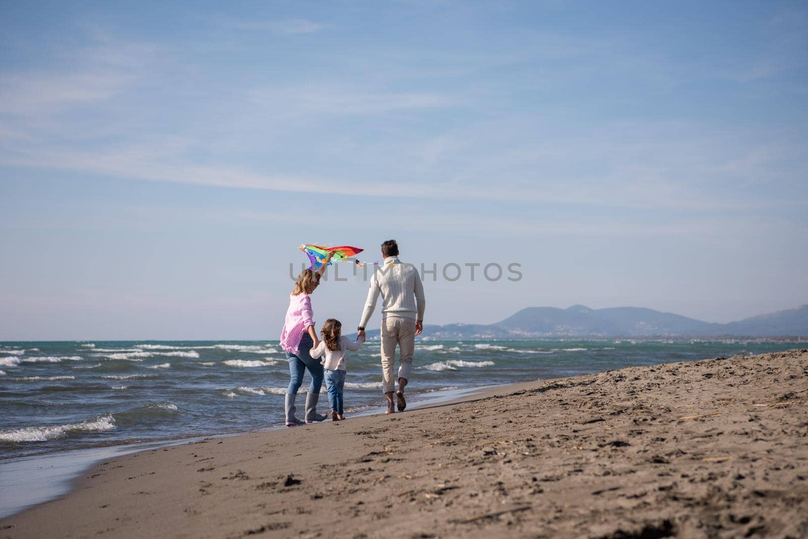 young family with kids resting and having fun with a kite at beach during autumn day