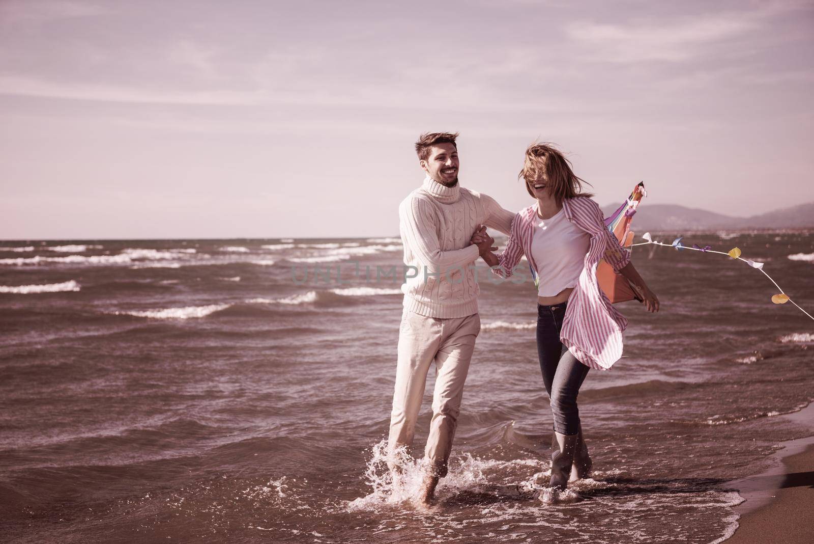 Young Couple having fun and Playing With A Kite On The Beach at autumn day filter