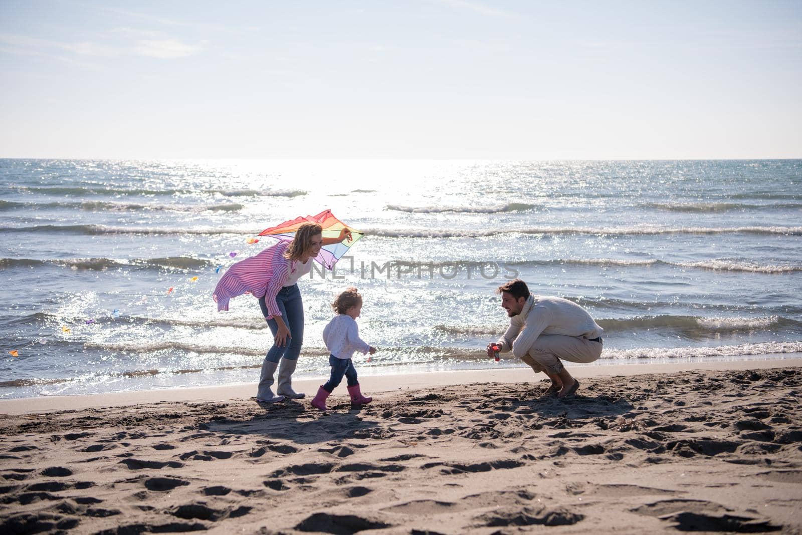 young family with kids resting and having fun with a kite at beach during autumn day