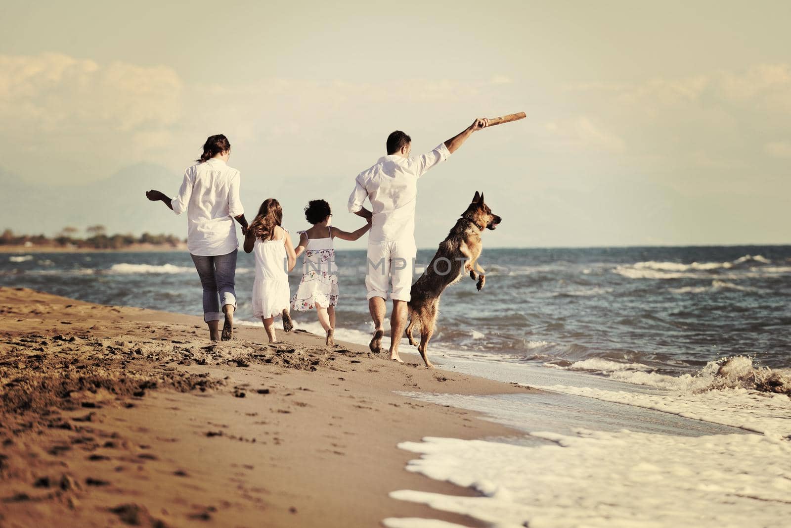 happy young family in white clothing have fun and play with beautiful dog at vacations on beautiful beach 