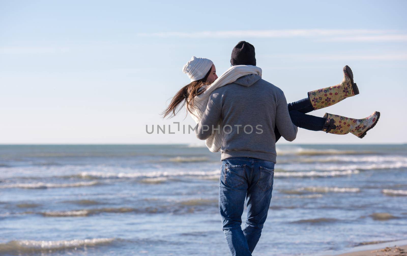 Young couple having fun walking and hugging on beach during autumn sunny day