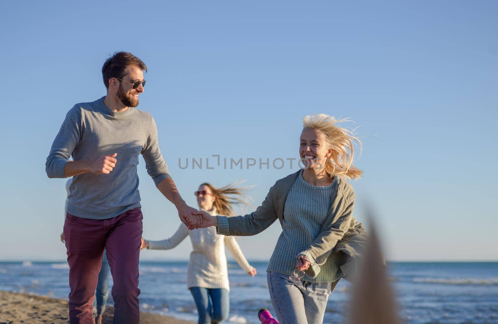 Group of friends running on beach during autumn day by dotshock