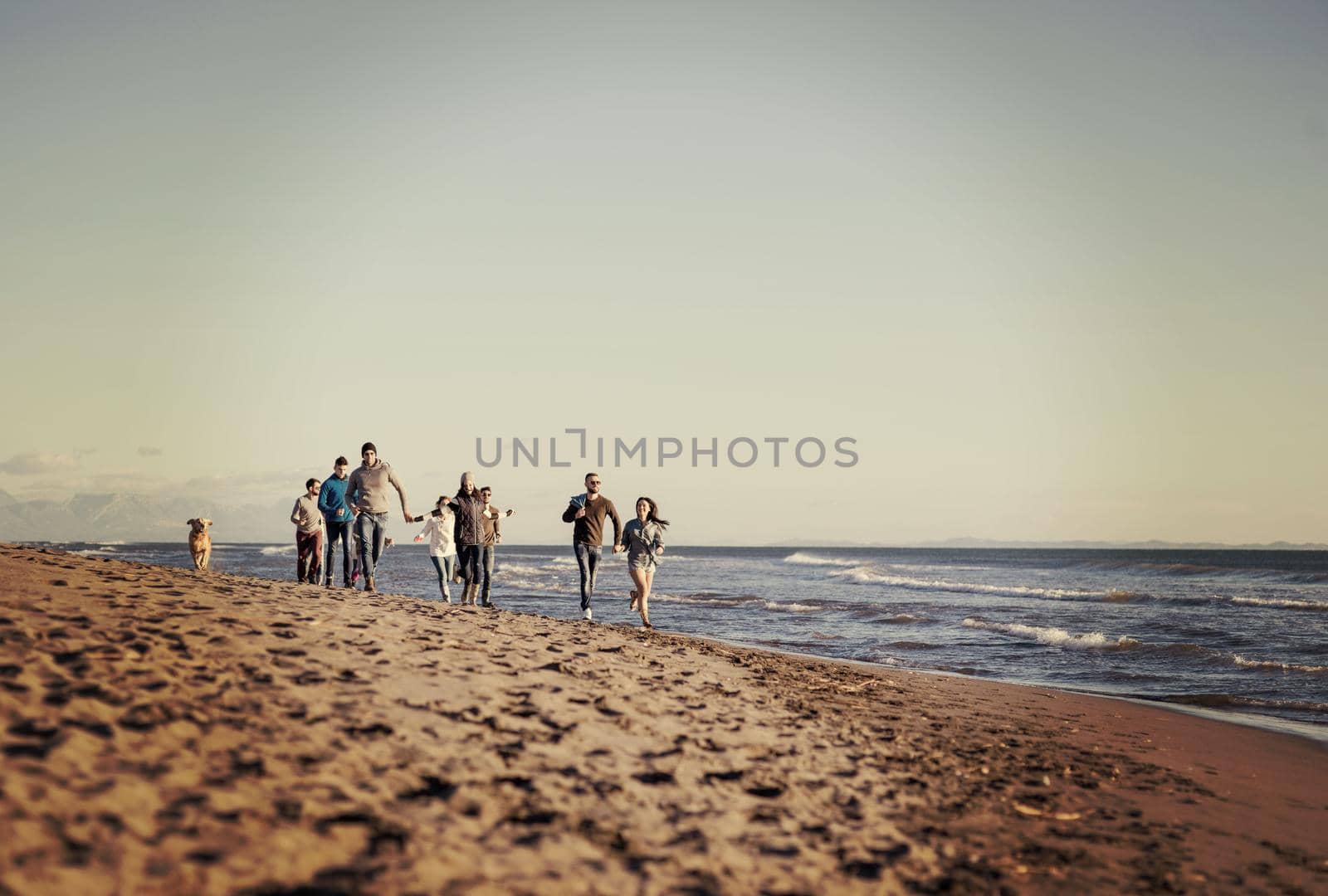 group of young friends spending day together running on the beach during autumn day colored filter