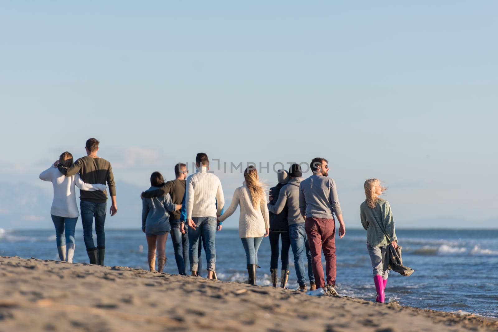 Group of friends running on beach during autumn day by dotshock