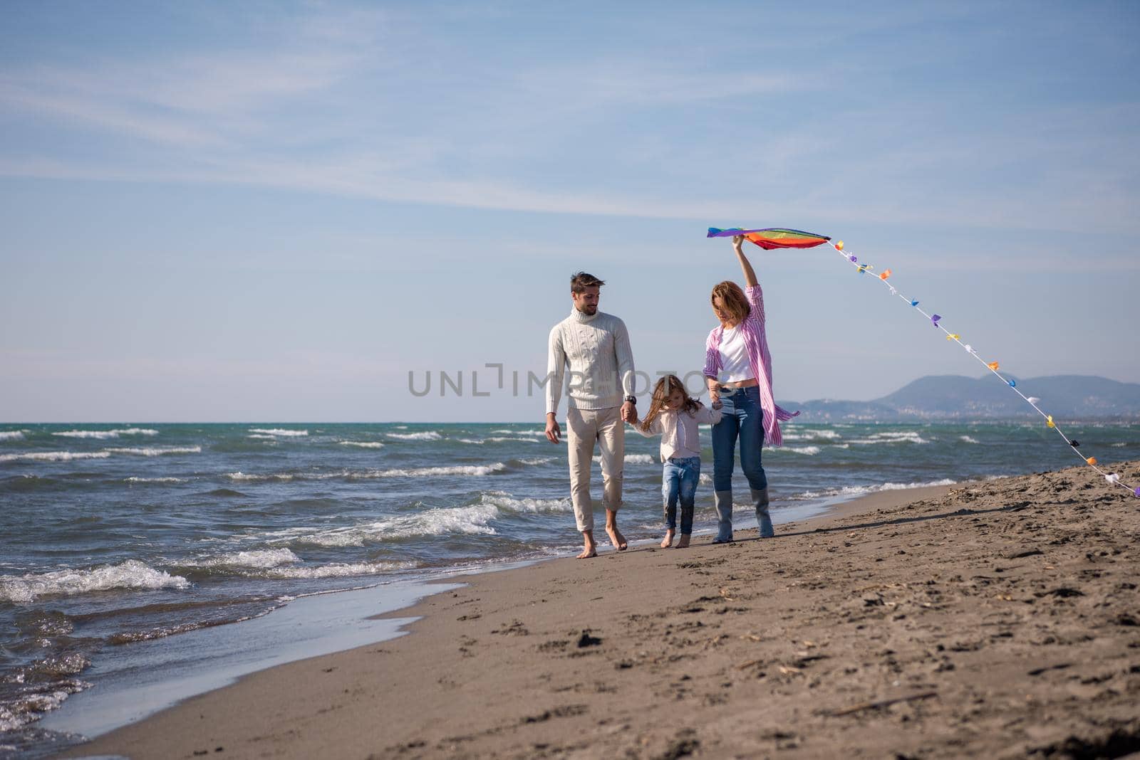 young family with kids resting and having fun with a kite at beach during autumn day