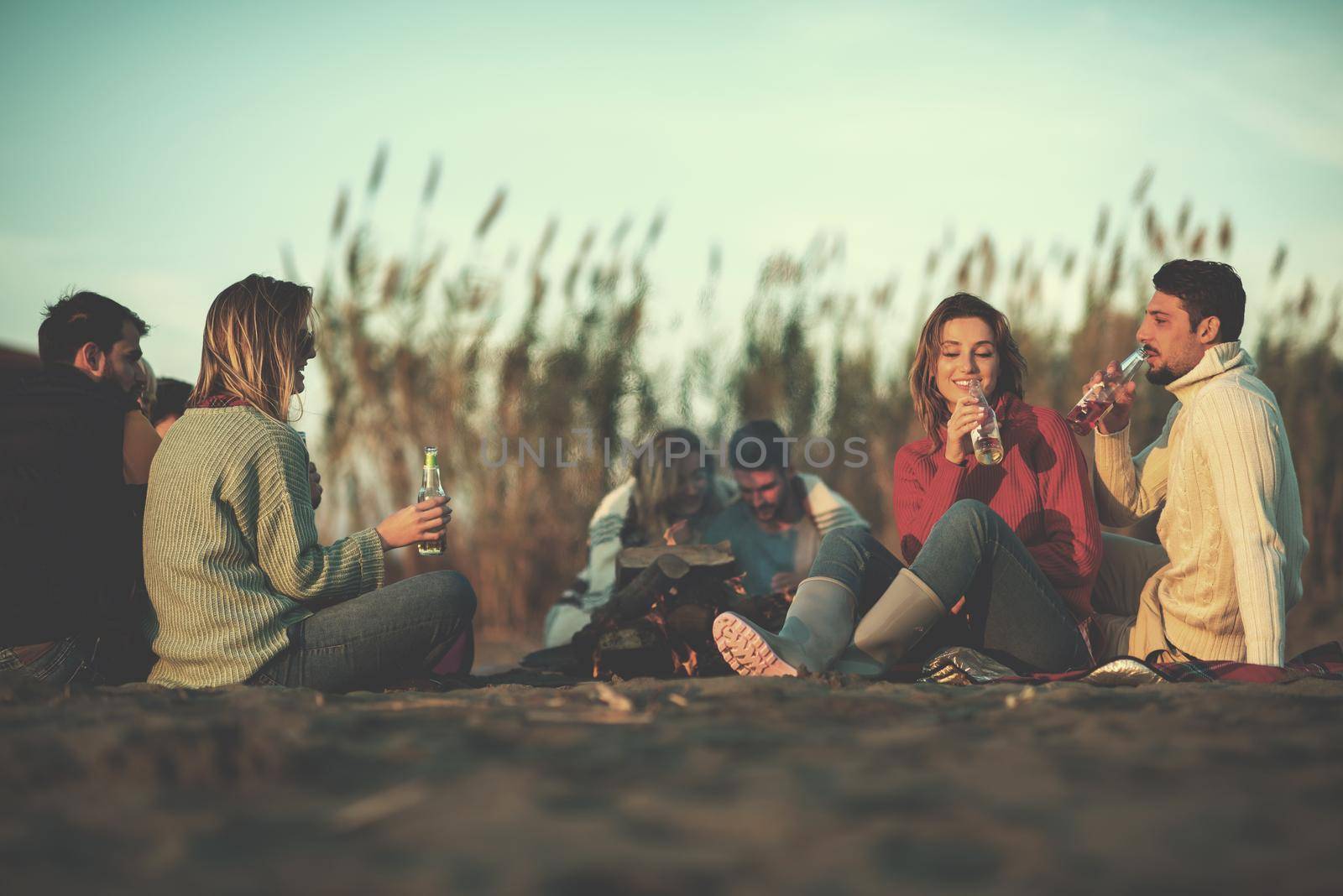 Young Couple enjoying with friends Around Campfire on The Beach At sunset drinking beer filter