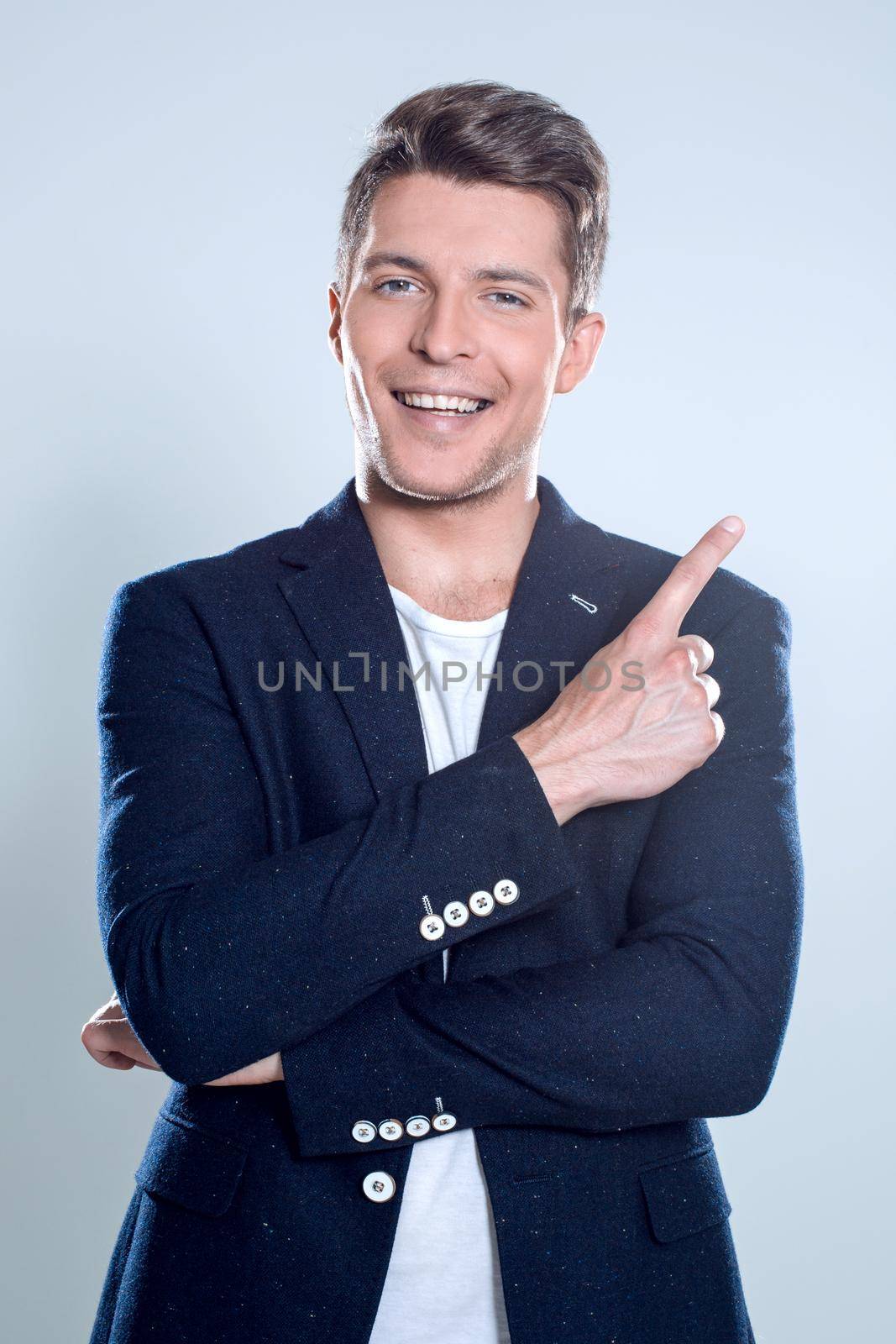 Close up portrait of young successful brunete stock-market broker guy on the gray background, he is smiling and is pointing on a copyspace with his finger