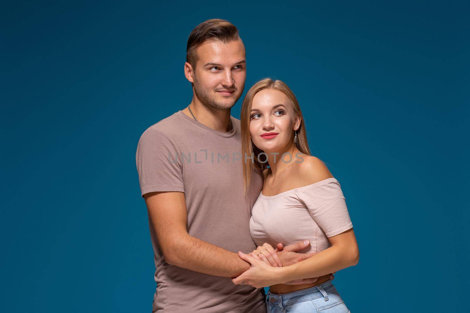 Young couple is hugging on blue background in studio. They wear T-shirts, jeans and smile. Friendship, love and relationships concept