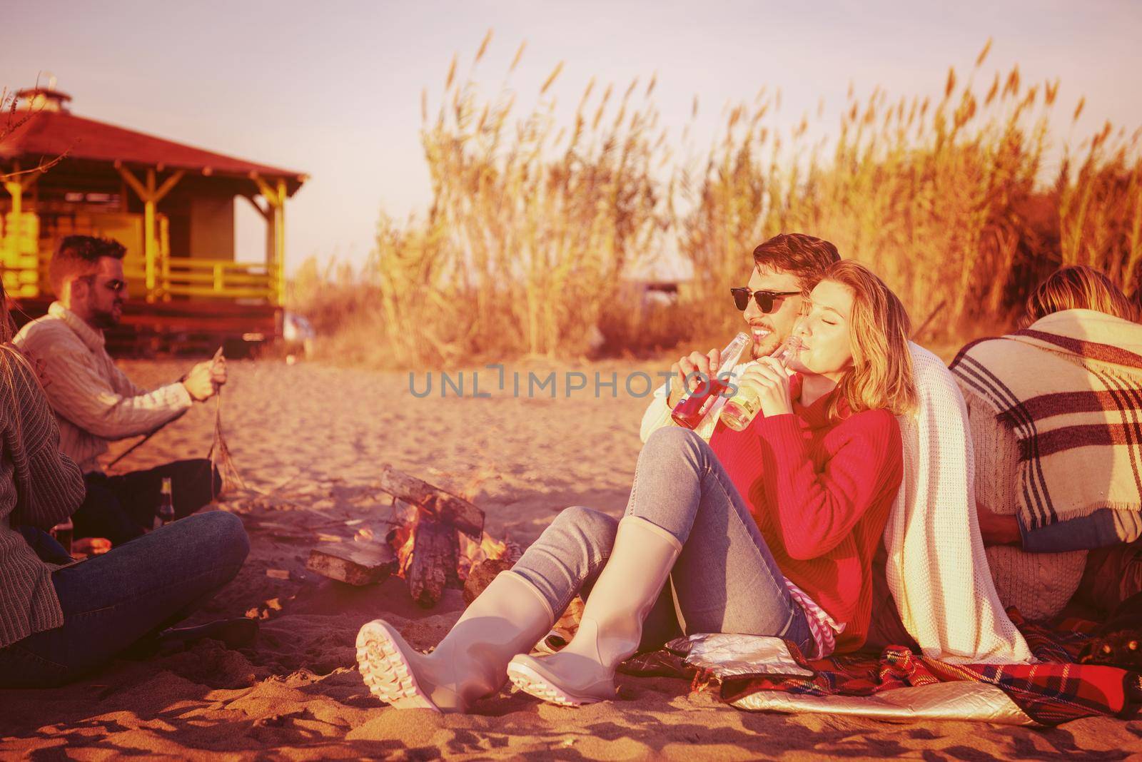 Young Couple enjoying with friends Around Campfire on The Beach At sunset drinking beer filter
